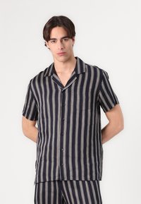 Camicia a maniche corte in navy con righe bianche verticali, dotata di apertura con bottoni, colletto a scollatura e una tasca sul petto. Tessuto dalla superficie liscia.