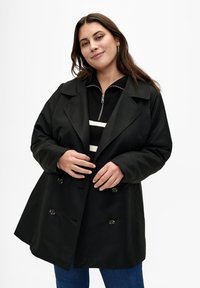 Černý dvouřadý trenčkot s širokými klopami a knoflíkovými detaily. Nositelný přes černý zip-up top s bílými pruhy. Hladká textura, volný střih.