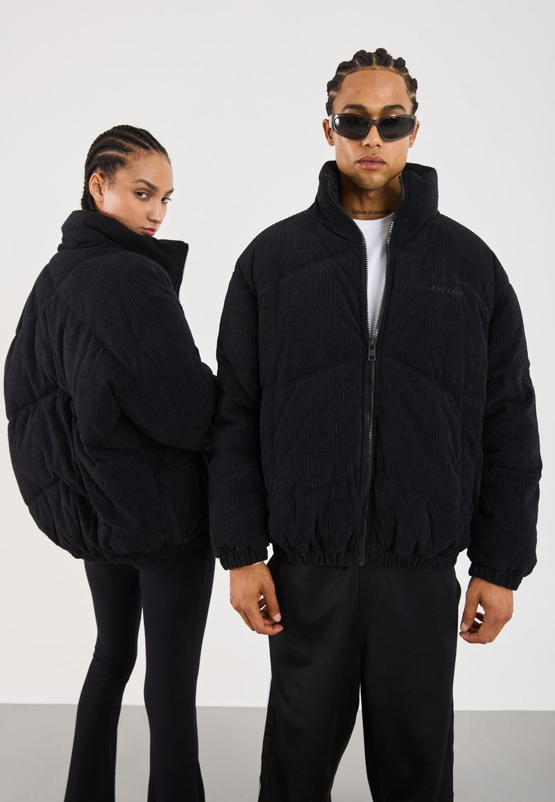 Veste rembourrée en velours côtelé noir avec fermeture à zip, texture matelassée et poignets et ourlet élastiques. Portée par deux mannequins, l'un tourné dans l'autre sens.