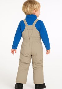 Beige sneeuwbroek voor kinderen met verstelbare bandjes, elastische tailleband en waterdicht materiaal, gedragen over een blauwe fleece top.