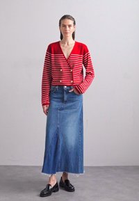 Rood gestreepte cropped cardigan met knopen, hoge taille denim rok met een split, en zwarte loafers. Effen achtergrond.