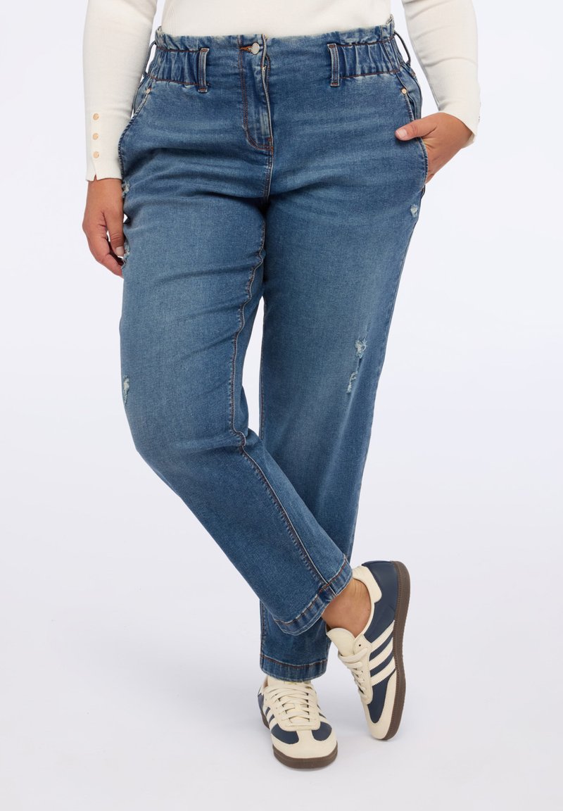 Blaue Jeans aus Denim mit lockerer Passform, ausgestattet mit einem gerafften Bund, subtilen Verwaschungen und dezenten Nähten. Kombiniert mit weißen und marineblauen Sneakers.