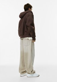 Overmaatse bruine hoodie van zachte stof, gecombineerd met losse, lichtgrijze jeans. Witte sneakers maken de casual look compleet.