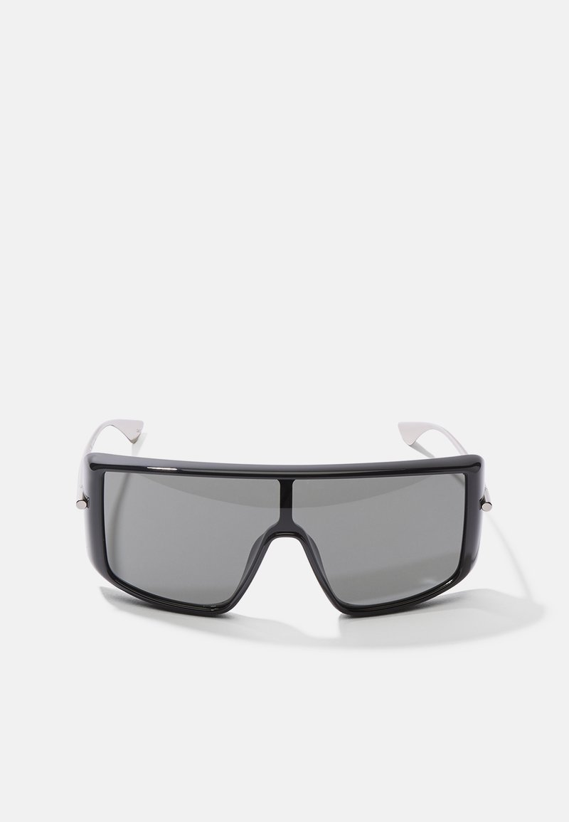 Sonnenbrille mit einer großen, rechteckigen Form. Schwarzes Kunststoffgestell mit dunkelgrauen Gläsern und weiß akzentuierten Bügeln. Elegantes Design.