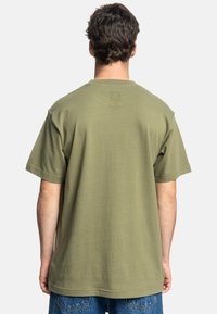 Olivgrünes Baumwoll-T-Shirt mit lockerer Passform, kurzen Ärmeln und Rundhalsausschnitt. Verfügt über ein dezentes Logo im oberen Rückenbereich.