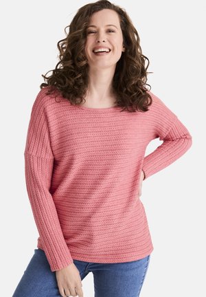 Rosa Strickpullover mit einem strukturierten, gerippten Design und einem weit geschnittenen Halsausschnitt. Lange, leicht lockere Ärmel; kombiniert mit blauen Jeans.