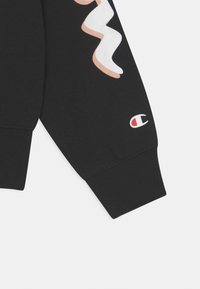 Black sweatshirt with a textured ribbed cuff. Features a colorful wavy design and a small Champion logo in red, white, and blue on the sleeve.