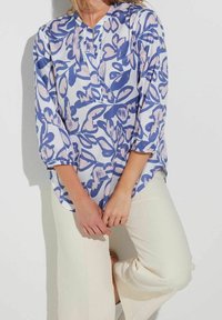 Blouse légère à motifs dans des tons de bleu et de rose avec un col rond et des manches trois-quarts, associée à un pantalon de couleur crème.