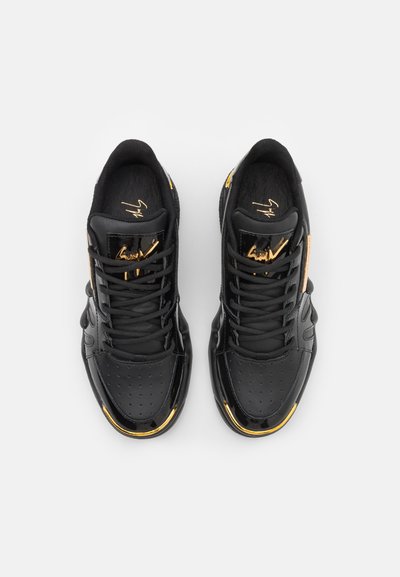 Baskets noires au design élégant, avec un bout en vernis, un tissu texturé, des accents dorés sur les côtés et des détails emblématiques sur la languette.