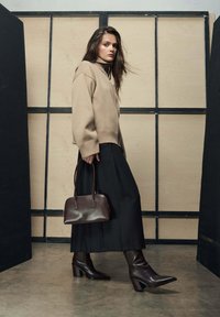 Beżowy dziergany sweter z wysokim kołnierzem, czarna zwiewna spódnica, brązowa skórzana torebka oraz brązowe kozaki na szpiczastym obcasie. Prosty i uporządkowany fason.