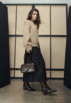 Beżowy dziergany sweter z wysokim kołnierzem, czarna zwiewna spódnica, brązowa skórzana torebka oraz brązowe kozaki na szpiczastym obcasie. Prosty i uporządkowany fason.