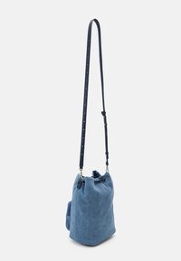 Sac seau en denim bleu avec une longue bandoulière noire réglable et une petite poche latérale sur fond clair.