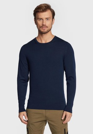 Maglione lavorato a maglia blu navy con scollatura rotonda e maniche lunghe. Presenta un design aderente e polsini a coste. Tessuto morbido e strutturato.