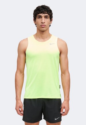 Homme portant un haut de sport sans manches dégradé jaune-vert et un short Nike noir, debout avec les bras détendus le long du corps sur un fond uni.