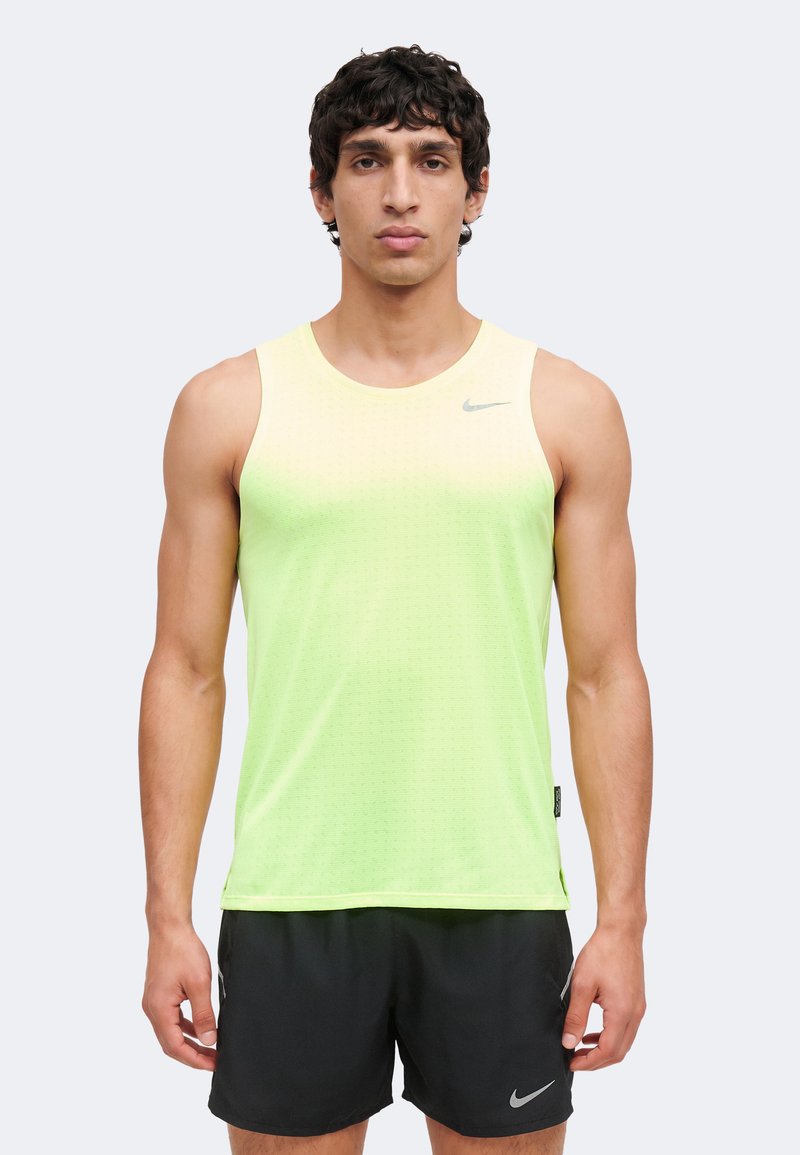 Homme portant un haut de sport sans manches dégradé jaune-vert et un short Nike noir, debout avec les bras détendus le long du corps sur un fond uni.