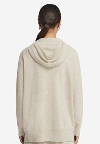 Beige huvtröja i mjukt tyg, med en avslappnad passform, ribbad fåll och nedhasade axlar, samt en synlig huva baktill.
