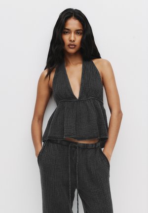 Haut halter texturé noir avec un décolleté plongeant et un design peplum, associé à un pantalon ample assorti avec un cordon de serrage réglable.
