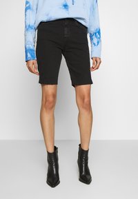 Mustat farkkushortsit, joissa on repaleinen helma, yhdistettynä vaaleansiniseen narutettu pulloveriin ja mustiin nilkkasaappaisiin, joissa on tyylikäs muotoilu ja istuva leikkaus.