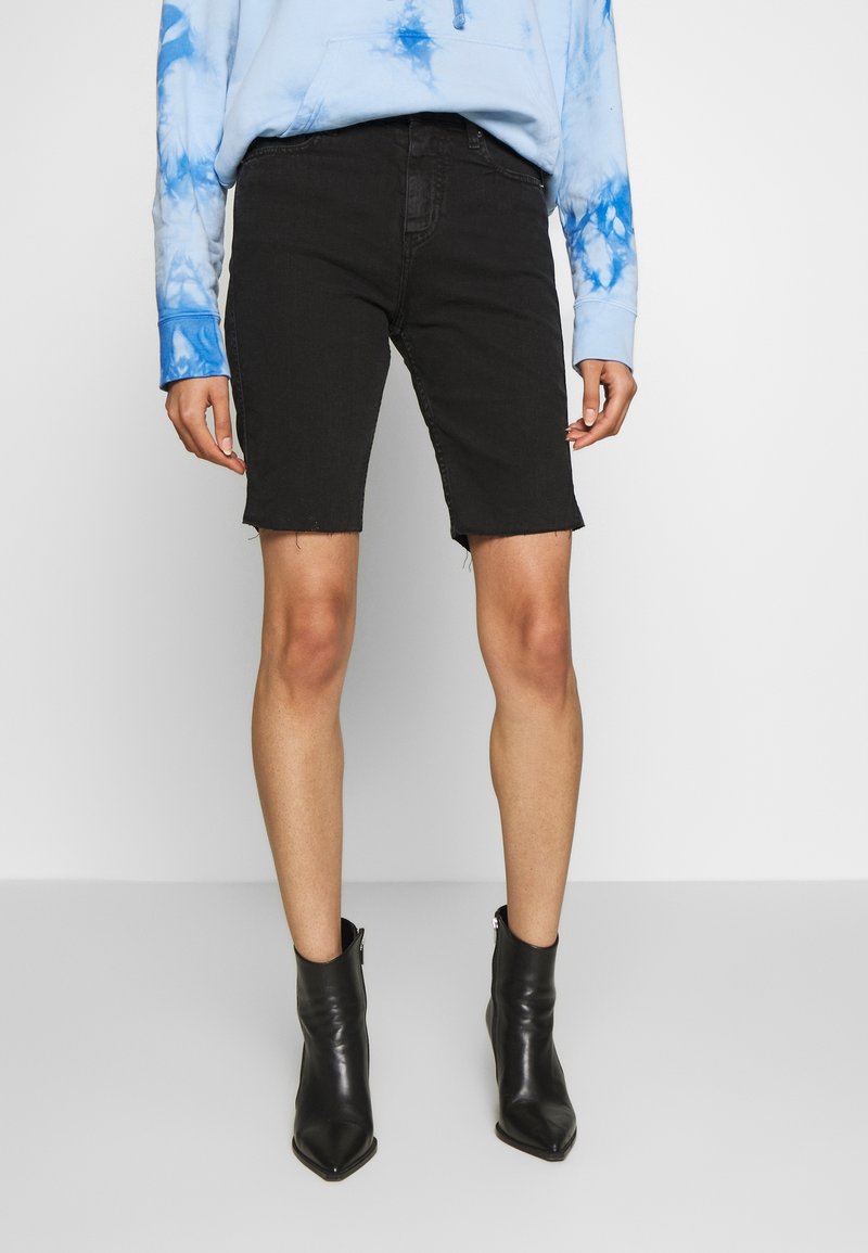 Mustat farkkushortsit, joissa on repaleinen helma, yhdistettynä vaaleansiniseen narutettu pulloveriin ja mustiin nilkkasaappaisiin, joissa on tyylikäs muotoilu ja istuva leikkaus.