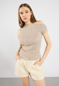 Beige avskuren topp med korta ärmar, med texturerade ränder. Matchad med ljusa shorts. Enkel och figurnära design.