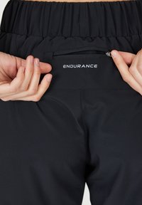 Svarta träningsbyxor har ett samlat midjeband och en liten ficka med blixtlås bak, där varumärket "ENDURANCE" visas.