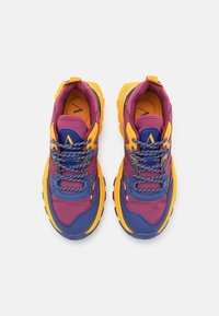 Purple, blue, and yellow athletic shoes with textured mesh and synthetic materials, featuring a multi-colored lace and thick yellow outsole.
