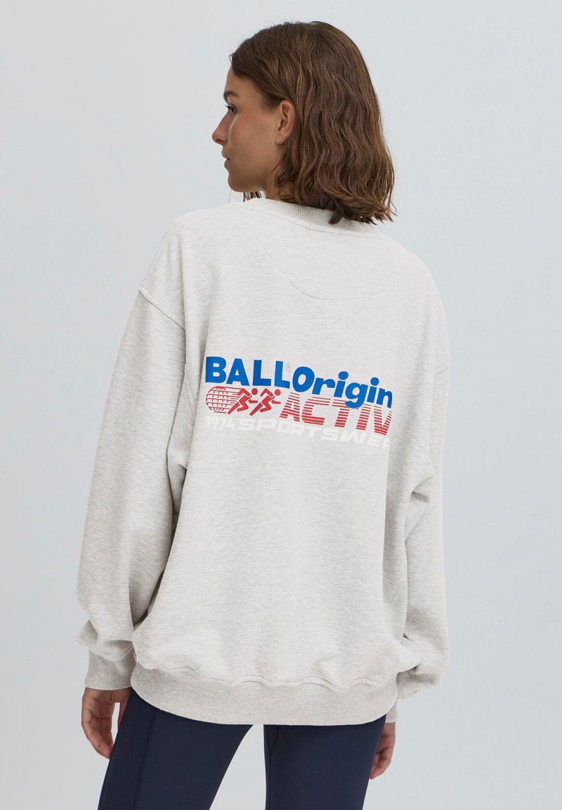 Szary sweatshirt z opadającymi ramionami, ściągaczami przy rękawach i u dołu. Na plecach znajduje się niebieski i czerwony napis, w tym "BALLorigin" i "ACTIVE."