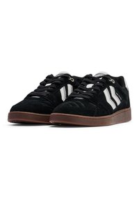 Schwarze Wildledersneaker mit weißen Akzenten, mit einer strukturierten Oberfläche, flachen Schnürsenkeln und einer braunen Gummisohle. Minimalistisches Design.