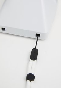 Gray rectangular device with rounded edges, textured surface, USB port, and a black cord with a circular black accent for attachment.