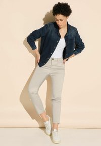 Dunkelblaue Jeanshemd mit langen Ärmeln, durchgeknöpfte Vorderseite, weißes Tanktop, beigefarbene figurbetonte Hose und weiße Turnschuhe. Einfaches und lässiges Outfit.