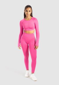 Eng anliegendes, rosa langärmeliges Crop-Top und hoch taillierte Leggings aus dehnbarem Material, kombiniert mit weißen Sneakers. Glatte Textur, nahtloses Design.