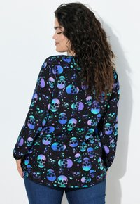 Schwarzes Langarmshirt mit mehrfarbigem Schädel- und Sternmuster, locker geschnitten und mit abgerundetem Saum, geeignet für legere Outfits.