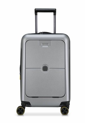 Maleta rígida plateada con forma rectangular, asa retráctil, dos ruedas con acentos amarillos y un sistema de cierre central.