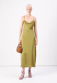 Olive green satin dress with a fitted bodice and spaghetti straps, reaching mid-calf. Paired with a brown woven handbag and purple heeled sandals.