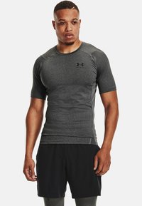 T-shirt de sport noir à manches courtes avec une finition grise texturée. Il présente un col rond et un logo Under Armour sur la poitrine.