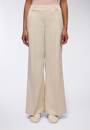 Pantaloni a gamba larga in tessuto beige chiaro con una texture liscia, dotati di un davanti piatto, passanti per la cintura e tasche laterali.