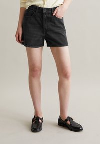 Zwarte denim shorts met een hoge taille, voorzakken en een knoopsluiting. Draagt met zwarte flats met een strap en decoratieve hardware.