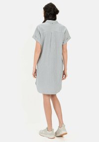 Gestreiftes Hemdkleid aus leichtem Material, mit kurzen Ärmeln und Kragen. Das Kleid hat einen geraden Schnitt und Seitenschlitze für Bewegungsfreiheit.