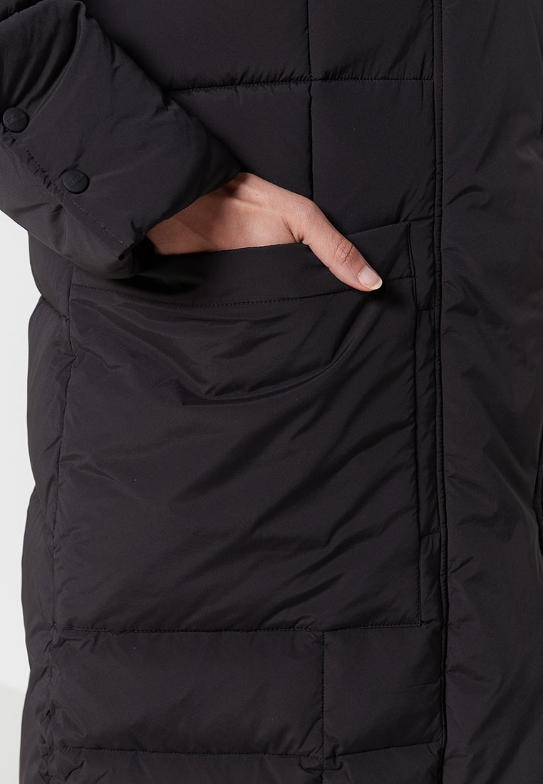 Schwarzer Puffer-Mantel mit gestepptem Design; verfügt über eine Seitentasche und ein Knopfmanschetten-Detail. Weiches, isoliertes Material für Wärme.