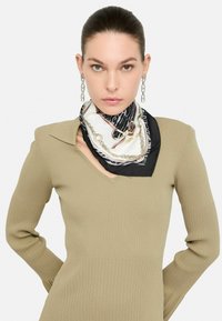 Seidenschal mit einer Mischung aus Schwarz-, Weiß- und Tierdruckmustern, versehen mit Kettenakzenten und einer glatten Textur, ums Hals getragen.