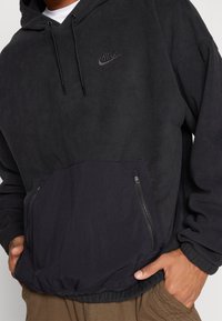 Svart fleecetröja med känguruficka, med dragkedjestängning och elastisk nederkant. Logotyp i svart på vänster bröst.