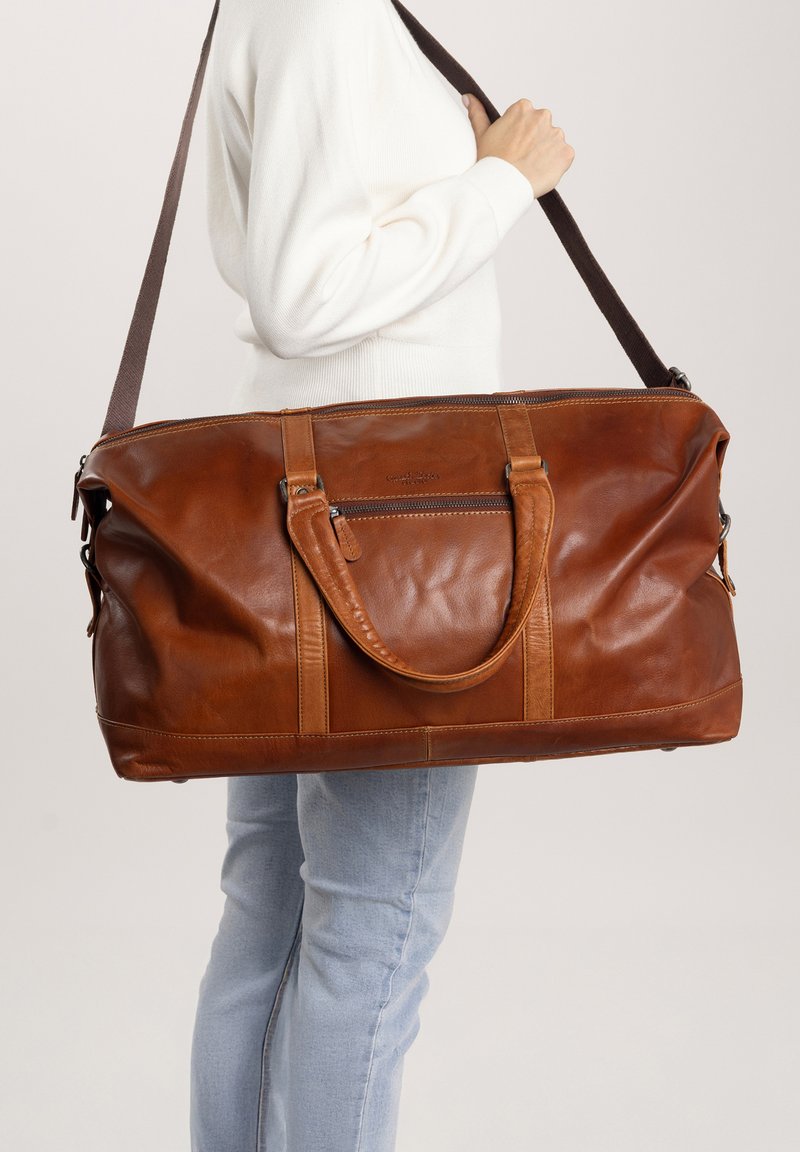 Borsa da viaggio in pelle marrone con cinturini beige a contrasto, parte superiore con zip e tasca frontale. Texture liscia e design spazioso per i viaggi.