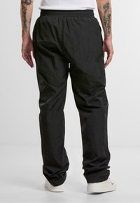 Pantalon de survêtement noir léger avec une taille élastique, des poignets froncés et une texture lisse. Porté avec des baskets blanches.