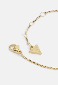 Collana in oro con ciondolo triangolare inciso "GUESS", chiusura a moschettone e maglie texturizzate.