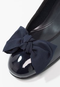 Ballerines en cuir laqué marine avec un nœud en tissu texturé au bout, forme ronde et ouverture élastique pour un maintien sécurisé.