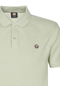 Polo shirt verde chiaro realizzato in tessuto testurizzato. Presenta una chiusura a tre bottoni e un patch circolare con logo in nero e rosso sul petto.