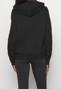 Sweat à capuche noir avec cordon de serrage à la capuche, poignets et ourlet côtelés, fabriqué en tissu doux. Le dos présente une finition lisse sans motifs.