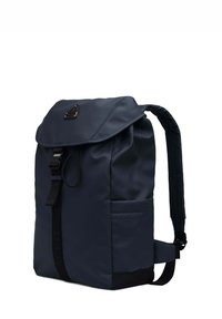 Zaino in nylon blu navy con flap pieghevole, spallacci regolabili, tasca frontale e hardware con marchio. Texture liscia con dettagli di cucitura.