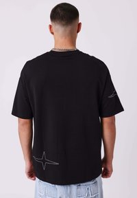 Zwarte katoenen T-shirt met korte mouwen, een relaxed fit en witte stervormige stikdetails op de onderrug.