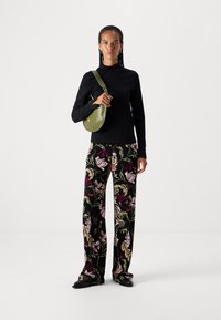 Schwarzes langärmliges Oberteil, weit geschnittene Hose mit floralen Mustern in Pink- und Grüntönen und eine kleine olivgrüne Umhängetasche.